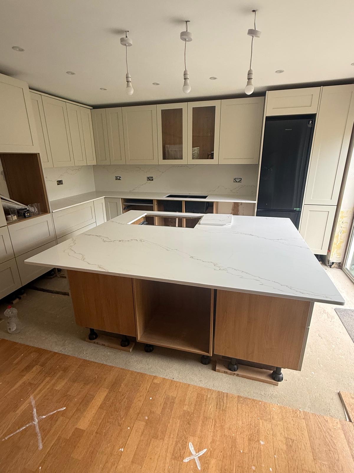 Large white quartz island with veining and cream cabinetry